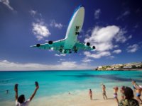 Now this is more like it! KLM 747 landing with a clear blue sky and the sun shining on the water giving it great colour and a nice shadow. Because of the distortion of the lens it looks like the plane is higher than it is but look at the tail and you&#39;ll see it really isn&#39;t very far off the water and then consider that the beach rises up to meet the runway level. I&#39;m not sure if the dipstick lower left is trying to sell his sandals or figuring he can touch the plane with just a few more inches of reach. Either way, he looks like an idiot.